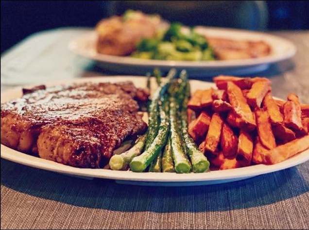 A grilled ribeye plated with grilled asparagus and sweet potato fries